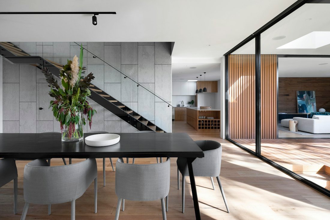 Open-plan dining room with natural wood finishes and a glass-walled living area